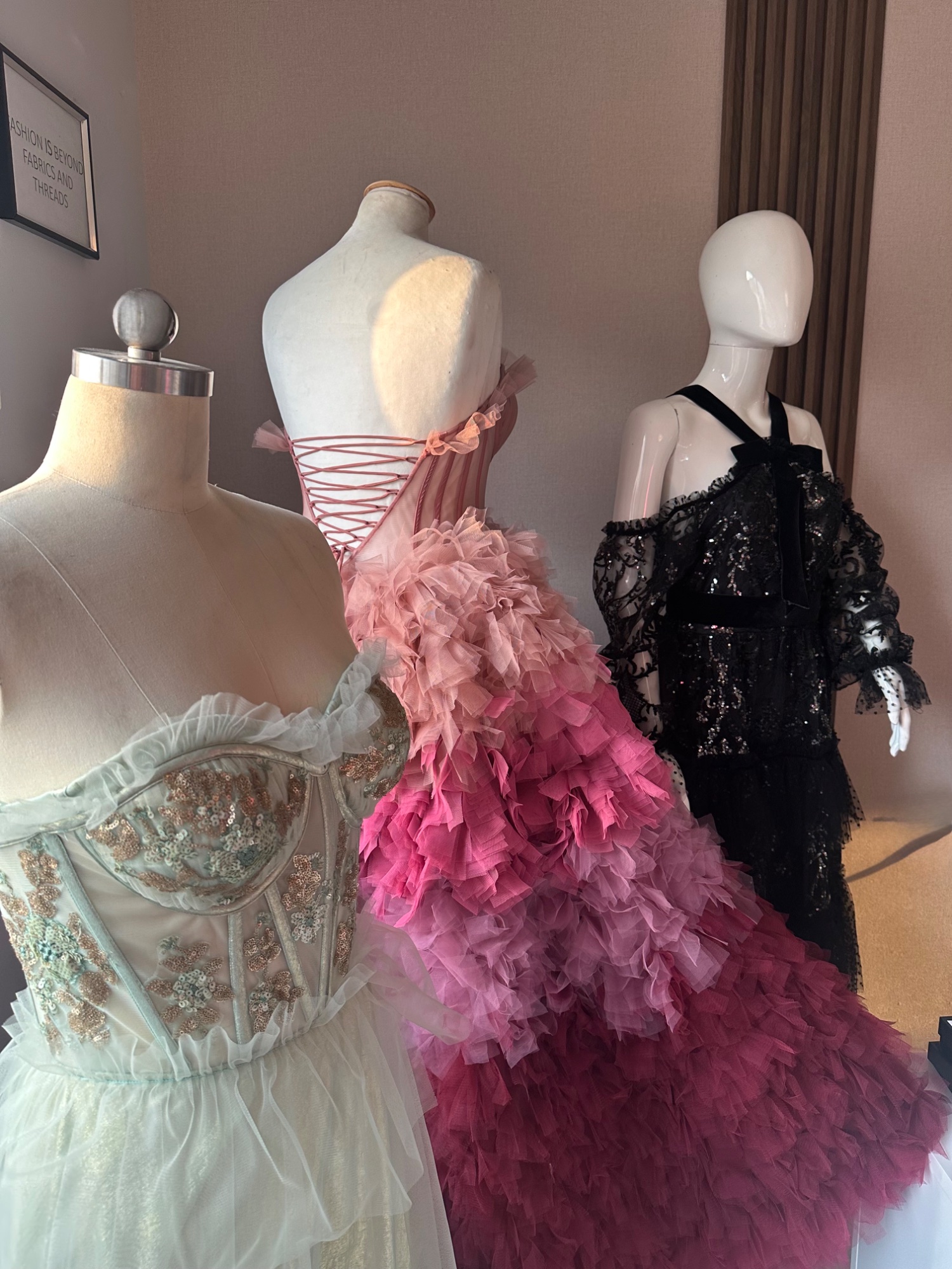 Three gowns on dress forms: a mint sequinned corset, a pink ombré tulle gown and a black lace dress